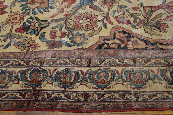 Distressed rug with intricate red and blue floral patterns on a faded beige field, bordered by dense medallions.