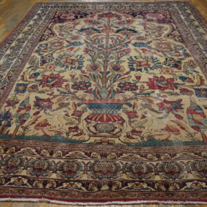 Low-pile rug with a detailed tree of life and bird pattern on a beige field, laid over wood planks.