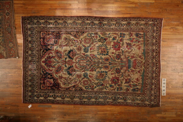Floral rug with a beige center and red and blue stylized motifs displayed flat on a hardwood floor.