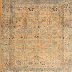 Golden tan rug with an elaborate blue and camel floral pattern and border on wood flooring.