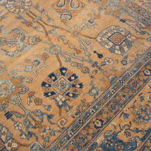 Low-pile rug with a camel background and an ornate traditional pattern of blue and terracotta florals.