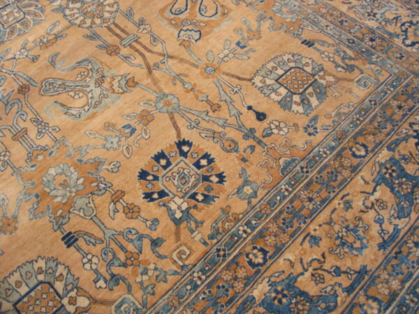Low-pile rug with a camel background and an ornate traditional pattern of blue and terracotta florals.