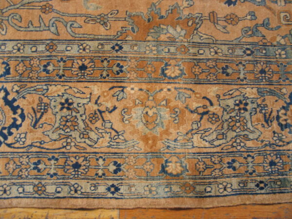 Close-up showing tan, blue, and sage green traditional floral patterns and borders on a wood floor.