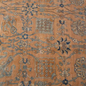 Low-pile rug in dusty peach featuring intricate blue, cream, and brown traditional botanical designs.