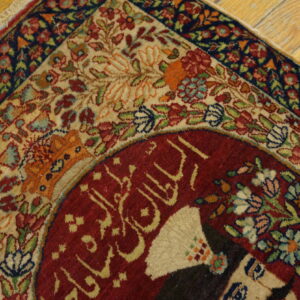 Detailed red, cream, and blue floral rug corner with script detail on distressed wood floor.