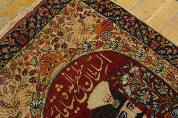 Detailed red, cream, and blue floral rug corner with script detail on distressed wood floor.