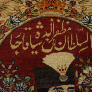 Ornate rug detail showing red calligraphy, part of a figure, and intricate cream and multicolored floral borders.