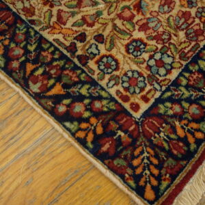 Traditional floral rug corner with a beige field and navy border rests on worn wooden floors.