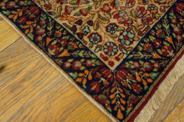 Traditional floral rug corner with a beige field and navy border rests on worn wooden floors.