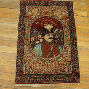 Detailed red and beige pictorial rug showing a portrait and script, bordered by florals, on worn wooden planks.