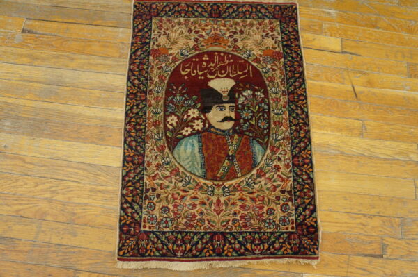Detailed red and beige pictorial rug showing a portrait and script, bordered by florals, on worn wooden planks.