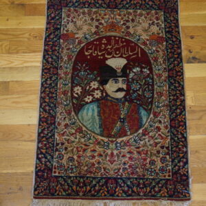 Red and blue highly detailed rug with a central portrait motif and script rests on wide plank wood flooring.