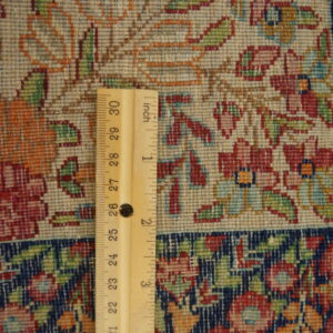 Close-up of a densely woven rug showing red and green floral motifs on a light ground, measured by a ruler.