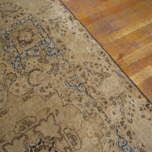 Distressed beige traditional rug with dark blue accents rests on wide plank wood flooring.