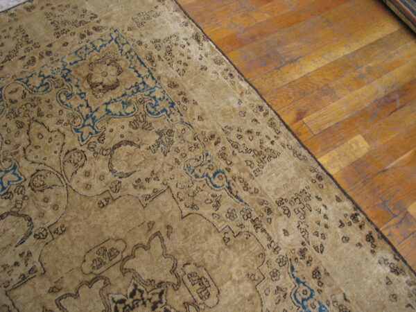 Distressed beige traditional rug with dark blue accents rests on wide plank wood flooring.