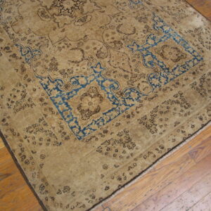 Distressed tan rug with dark brown and bright blue traditional motifs on plank hardwood flooring.