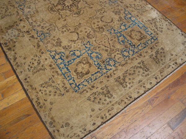 Distressed tan rug with dark brown and bright blue traditional motifs on plank hardwood flooring.