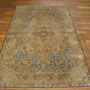 Tan and dark brown traditional rug with blue spandrels displayed on light brown hardwood flooring.