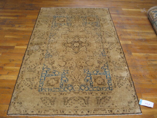 Tan and dark brown traditional rug with blue spandrels displayed on light brown hardwood flooring.