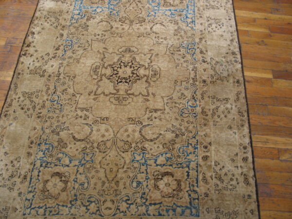 Tan and dark brown traditional rug with bright blue accents lies on wood plank flooring.