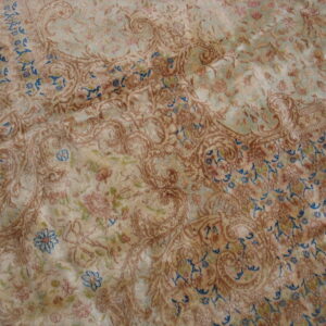 Close-up of a low-pile, ornate rug with distressed tan, blue-green, and blue floral and paisley patterns.