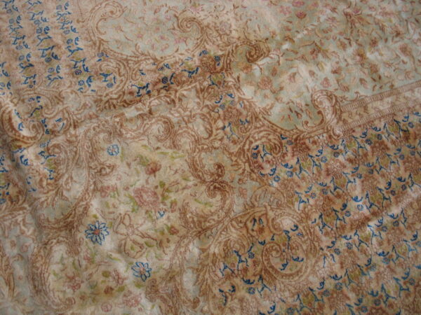 Close-up of a low-pile, ornate rug with distressed tan, blue-green, and blue floral and paisley patterns.
