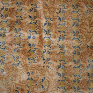 High-pile rug showing an intricate pattern in beige, rust, and bright blue floral motifs.
