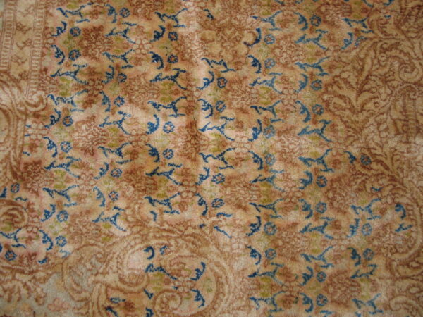 High-pile rug showing an intricate pattern in beige, rust, and bright blue floral motifs.
