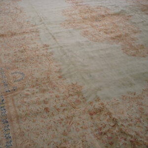 Muted green rug showing a dense traditional floral pattern in faded tan and rose colors.