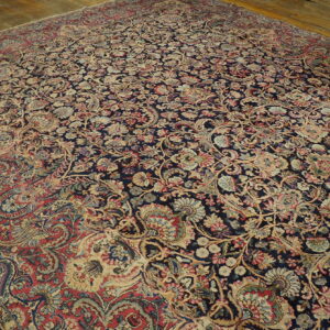 Dense navy rug with faded red, beige, and blue floral and vine patterns lying on light wood flooring.