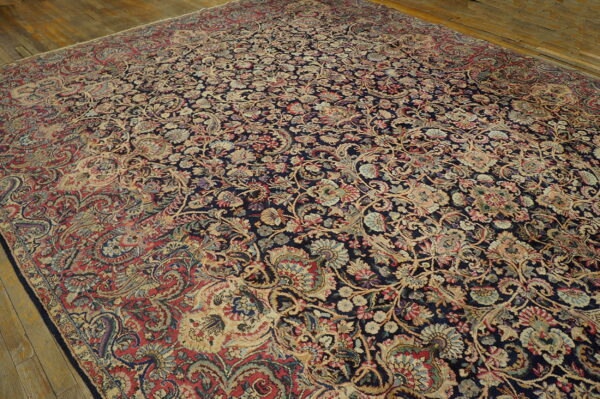 Dense navy rug with faded red, beige, and blue floral and vine patterns lying on light wood flooring.