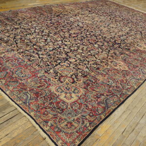 Ornate navy and red floral rug with low pile lying on rough, pale wooden plank flooring.
