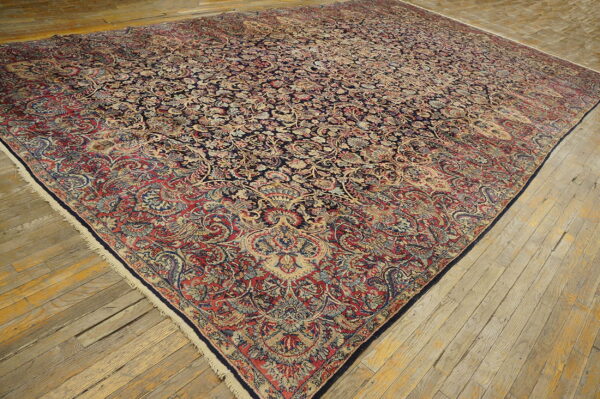 Ornate navy and red floral rug with low pile lying on rough, pale wooden plank flooring.