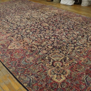 Large traditional rug with dense navy, red, and beige floral patterns on worn wood floorboards.