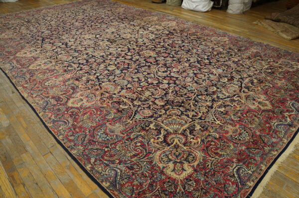 Large traditional rug with dense navy, red, and beige floral patterns on worn wood floorboards.