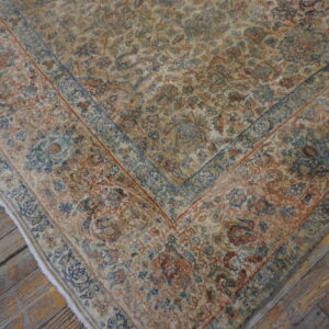 Distressed beige rug featuring complex floral motifs in rust and blue, lying on weathered wood planks.