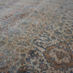 Muted beige rug surface with a dense traditional floral pattern in navy, rust, and teal accents.