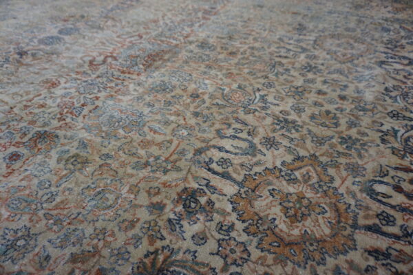 Muted beige rug surface with a dense traditional floral pattern in navy, rust, and teal accents.