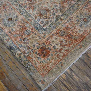 Muted beige rug corner with complex red-orange and blue traditional designs on rustic wood flooring.