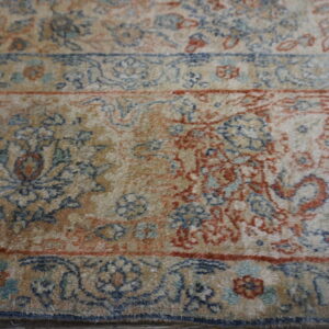 Muted, high-pile rug detail featuring traditional floral designs and multiple borders in tan, blue, and red.