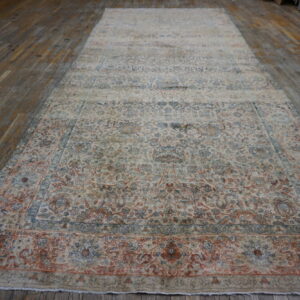 A large, distressed traditional rug in ivory, blue, and terracotta lies flat on a worn wood plank floor.