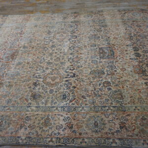 Overhead view of a large, faded floral patterned rug in cream, blue, and rust tones on wooden planks.