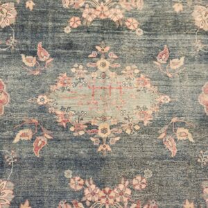 Close-up of a low-pile rug with a faded teal field and traditional pink and peach floral patterns.