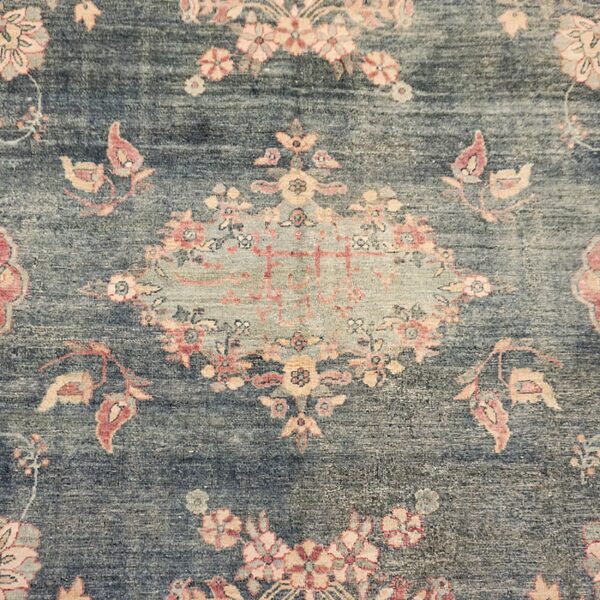 Close-up of a low-pile rug with a faded teal field and traditional pink and peach floral patterns.