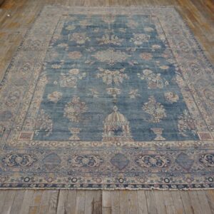 Muted indigo rug featuring complex floral and architectural designs rests on worn wood floorboards.