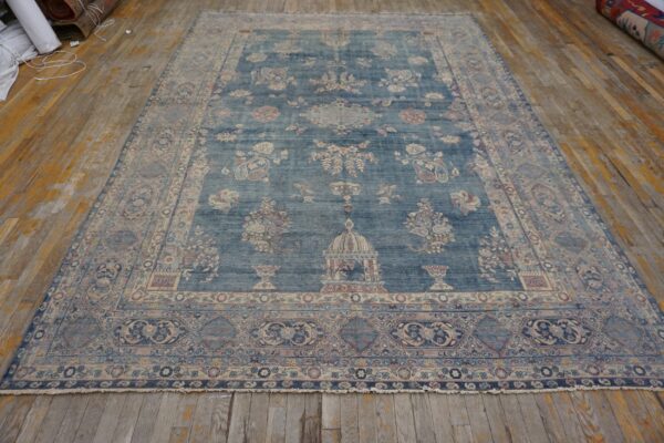 Muted indigo rug featuring complex floral and architectural designs rests on worn wood floorboards.