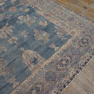 Distressed blue rug featuring beige and pink traditional floral patterns lies on worn wood planks.
