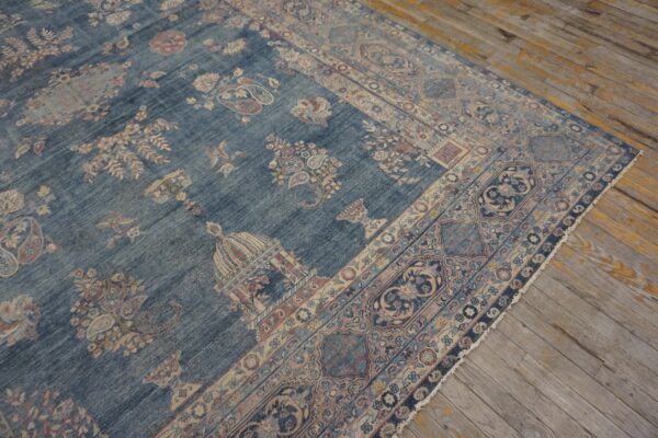 Distressed blue rug featuring beige and pink traditional floral patterns lies on worn wood planks.