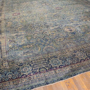 Distressed blue and teal rug with intricate traditional patterns rests on light brown wood planks.