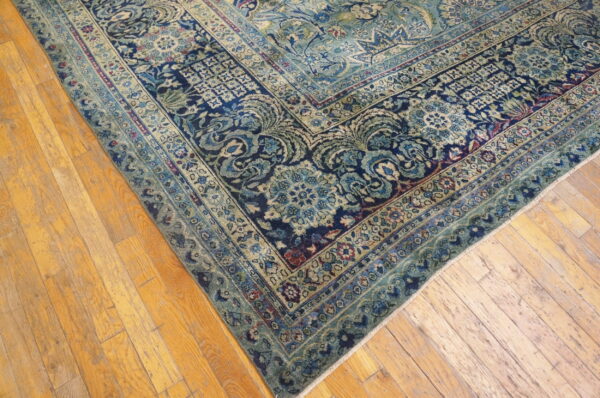 Detailed view of a navy, teal, and cream traditional floral rug corner on distressed wood flooring.